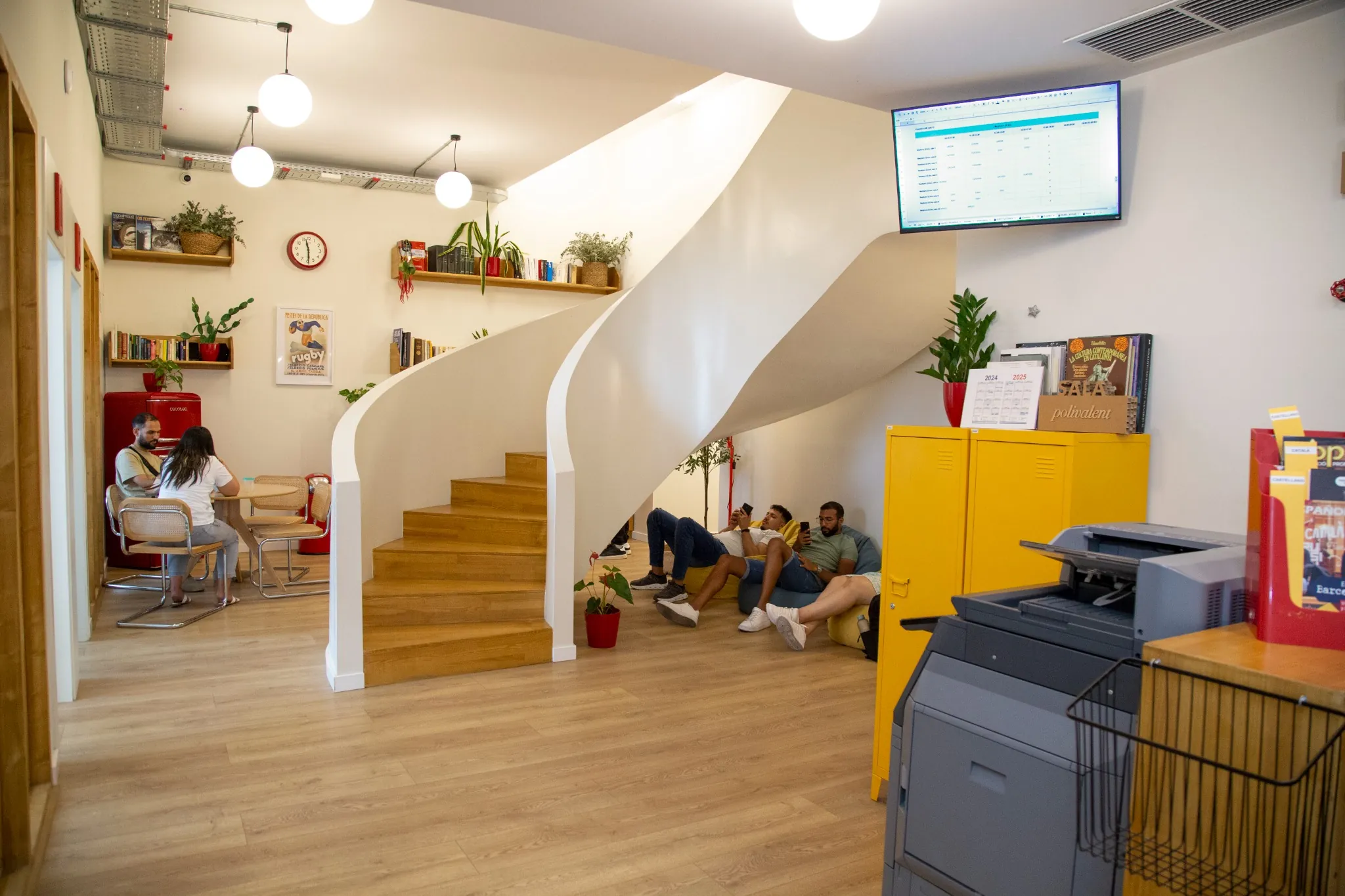 Zona común interior de la escuela de idiomas BCNLIP UP en Barcelona con biblioteca, estudiantes y escaleras modernas.