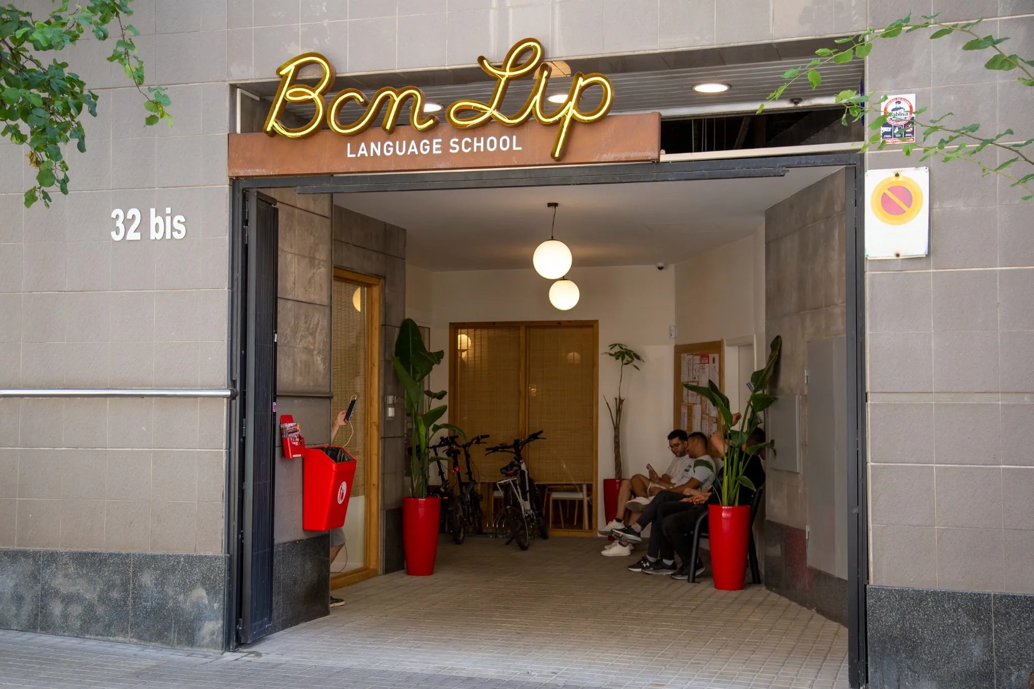 Fachada exterior de la escuela BCNLIP UP en Barcelona con cartel luminoso y estudiantes en la entrada.