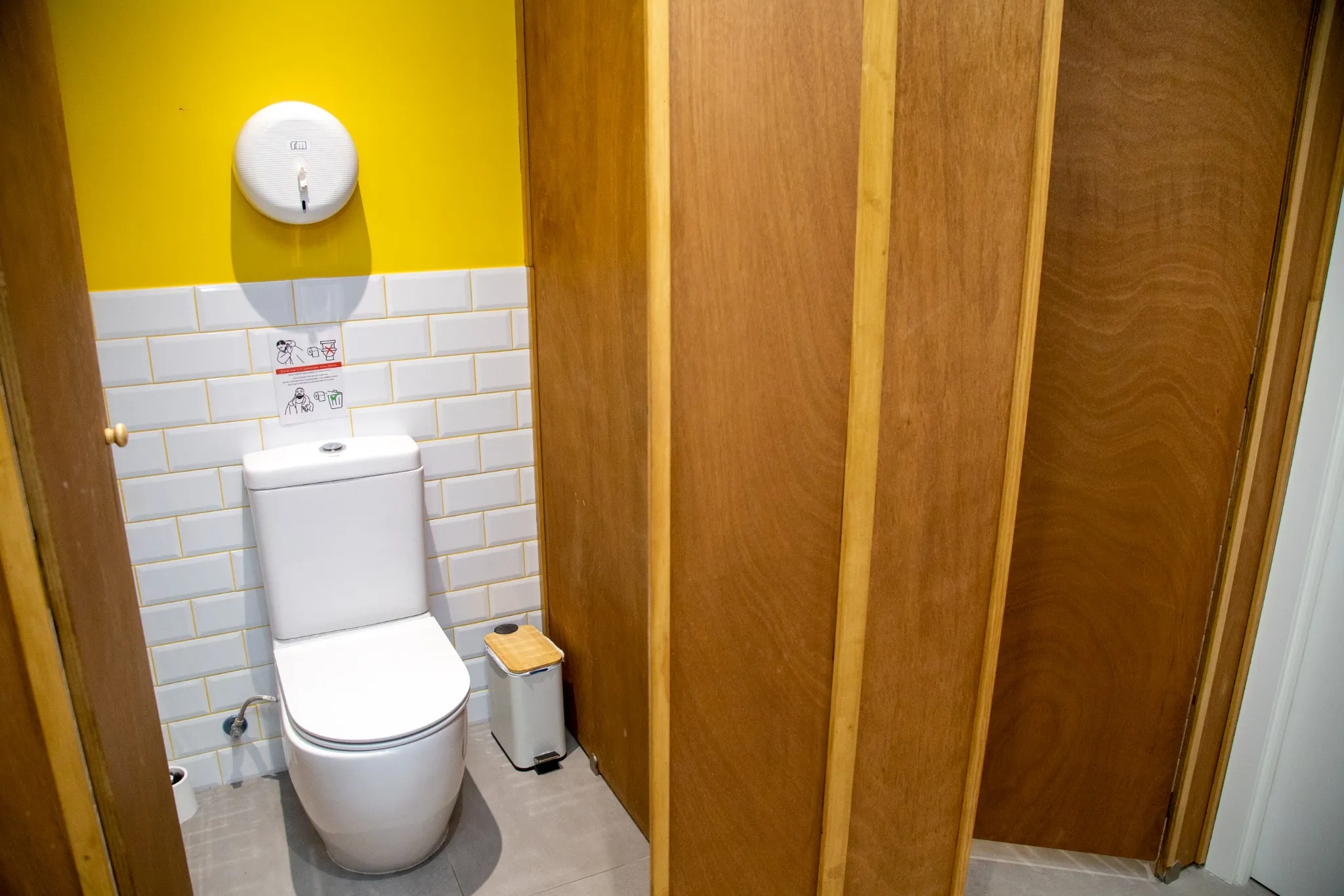 Baño moderno de la escuela de idiomas BCNLIP UP en Barcelona, con inodoro, papelera y señalización educativa.